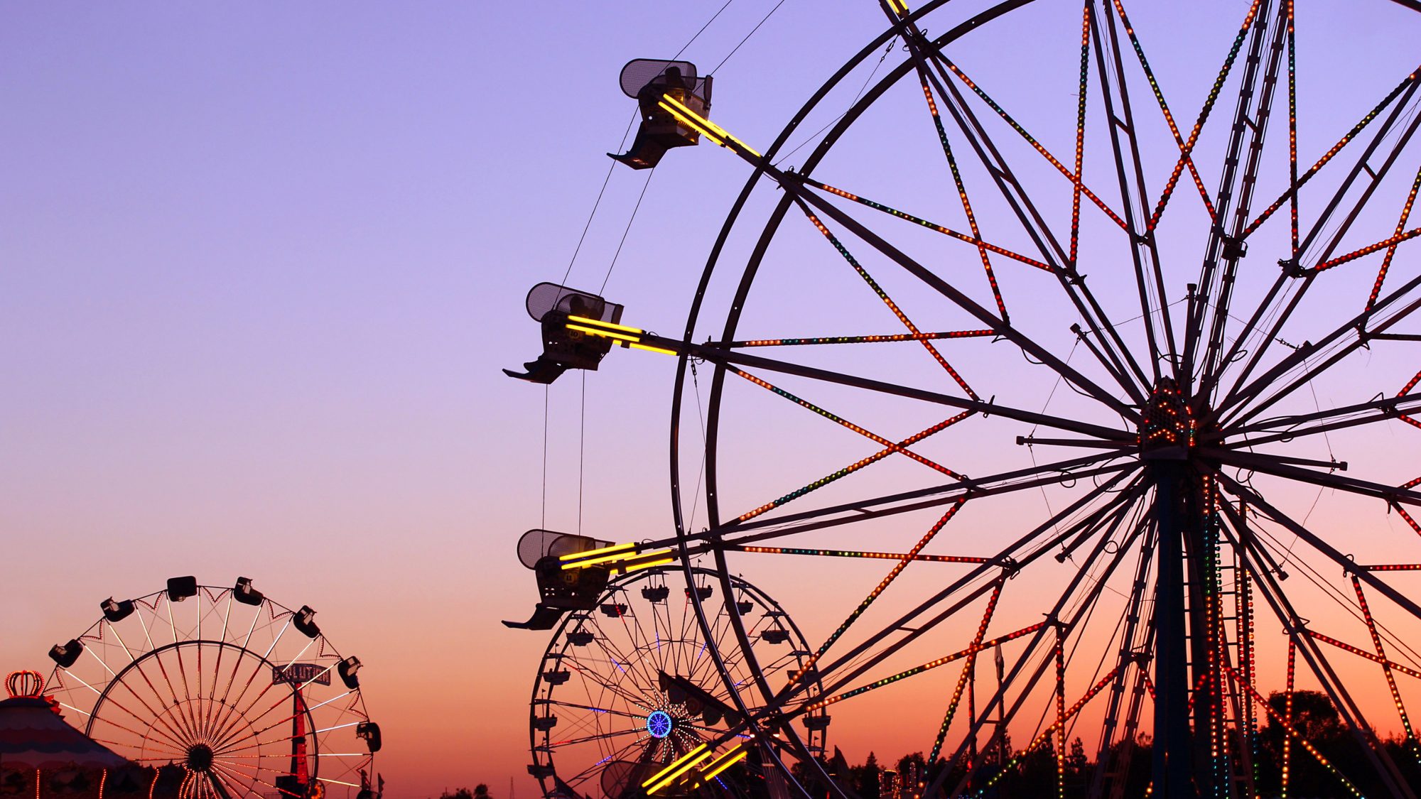 Ferris wheels lit up against a sunset sky at the county fair
